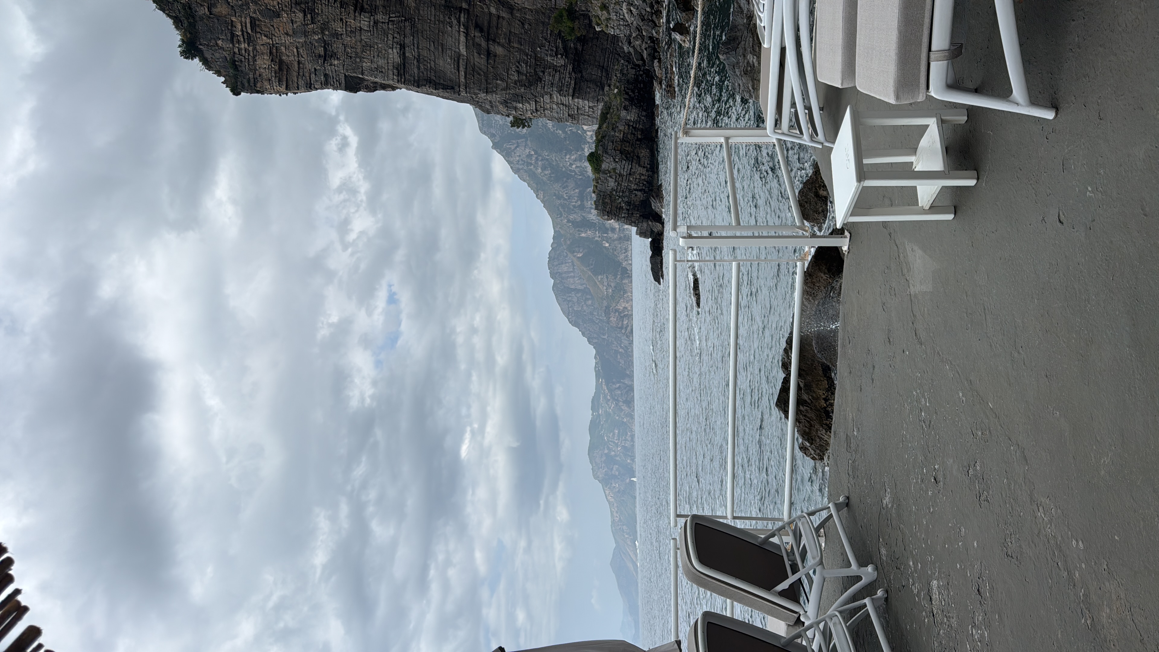 White sun loungers on the private beach with dramatic cliff and cloudy sky