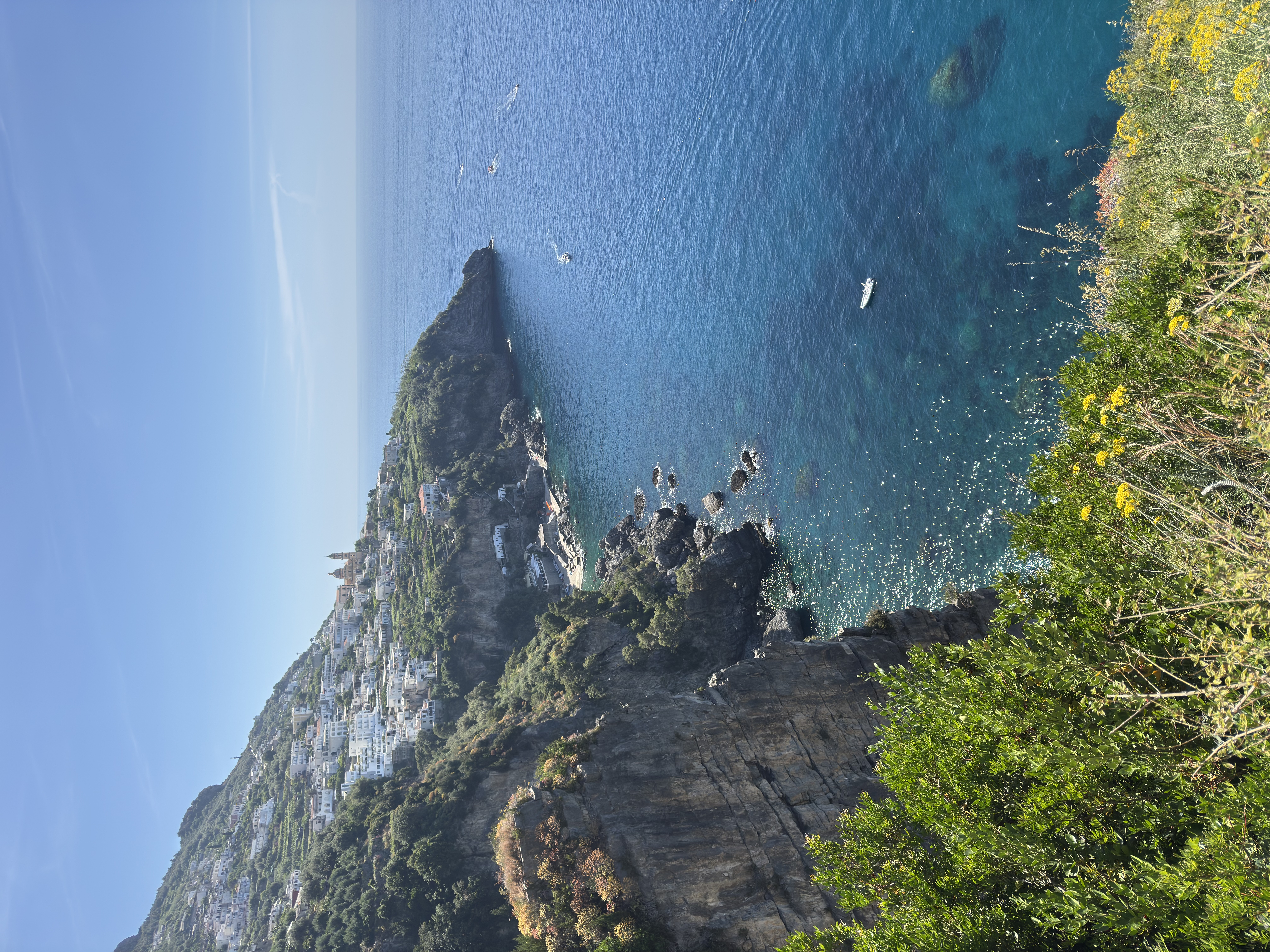 Amalfi Coast cliff with turquoise water and wildflowers in early May